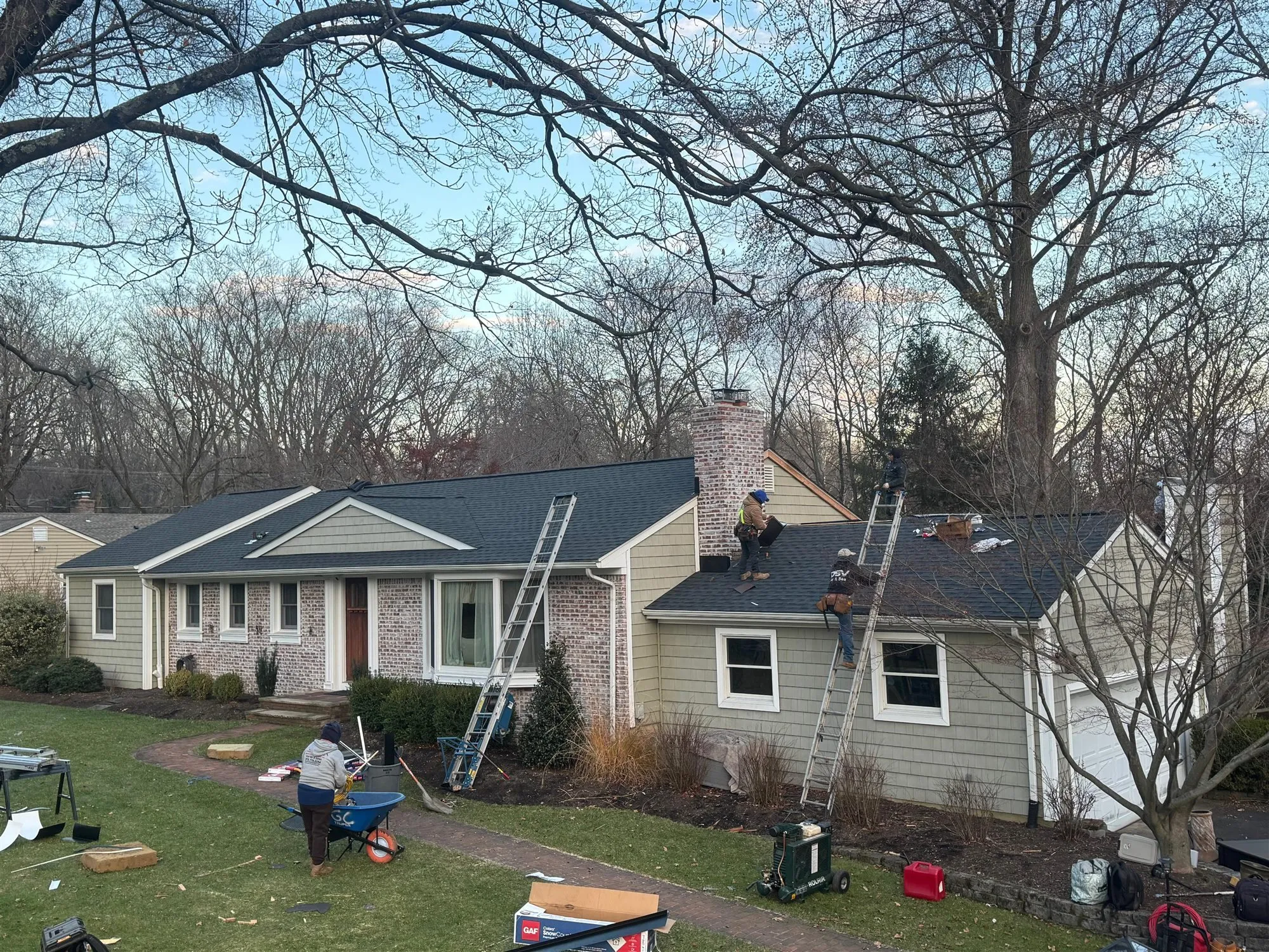 Imperial roofers installing shingles on a ranch house with a brick chimney